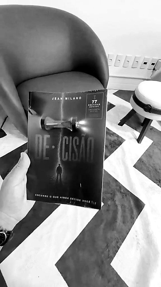 O livro DE·CISÃO lacrado, com a ampulheta oficial dentro da embalagem