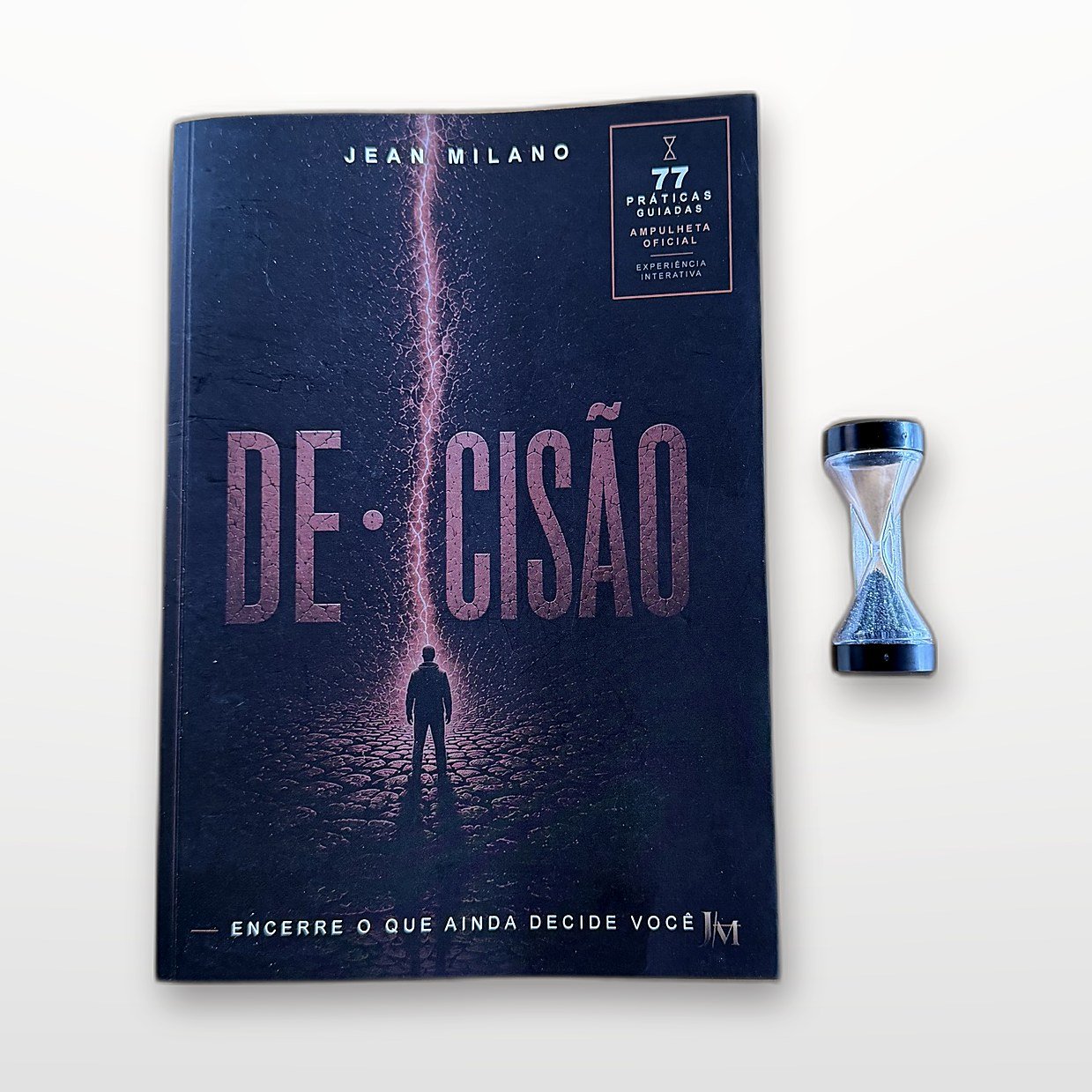O livro DE·CISÃO sobre a mesa, com a ampulheta oficial ao lado